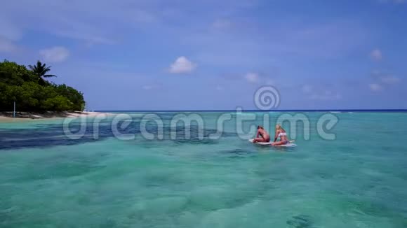 两个漂亮的年轻女孩坐在冲浪板上在温暖的蓝色海水中鸟瞰视频的预览图