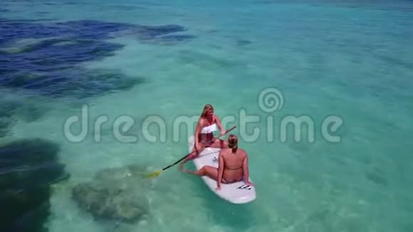 V08185两个漂亮的年轻女孩坐在冲浪板上在温暖的蓝色海水中鸟瞰天空视频的预览图