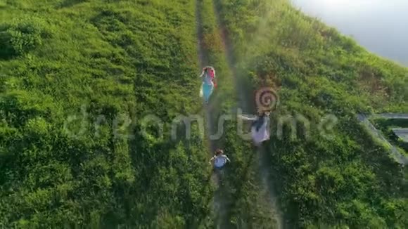 空中景色快乐的男孩和女朋友手里拿着彩带在河边的草地上奔跑视频的预览图