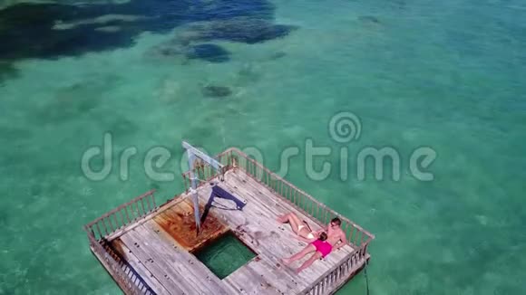 两个年轻人在浮筒上进行浪漫的日光浴在美丽清澈的水蓝色海水中鸟瞰视频的预览图