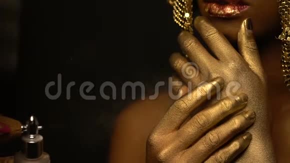化妆师正在把金色的喷雾喷在美丽迷人的非洲女人的身上她的嘴唇是红色的光泽视频的预览图