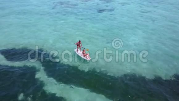 V08361两个漂亮的年轻女孩坐在冲浪板上在温暖的蓝色海水中鸟瞰天空视频的预览图