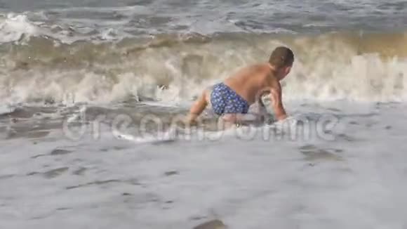 宝贝在海滩上在海浪中在金沙上玩冲浪的男孩头盖着孩子的波浪视频的预览图