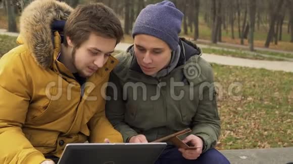 学生们使用笔记本电脑和平板电脑坐在公园的长凳上视频的预览图
