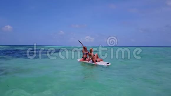 V08397两个漂亮的年轻女孩坐在冲浪板上在温暖的蓝色海水中鸟瞰天空视频的预览图