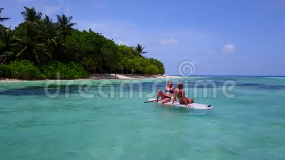 V08396两个漂亮的年轻女孩坐在冲浪板上在温暖的蓝色海水中俯瞰空中景色视频的预览图