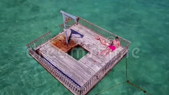 V08590两个年轻人在浮舟上浪漫地日光浴在美丽清澈的水蓝色海水中鸟瞰视频的预览图