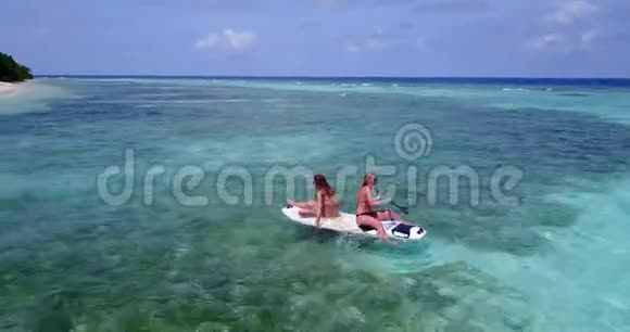 V08304两个漂亮的年轻女孩坐在冲浪板上在温暖的蓝色海水中鸟瞰天空视频的预览图