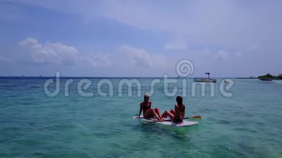 V08174两个年轻漂亮的女孩坐在冲浪板上在温暖的蓝色海水中俯瞰空中景色视频的预览图