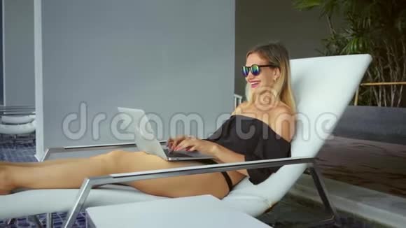 自由职业者妇女坐在游泳池附近的休息室里在笔记本电脑上工作动作缓慢视频的预览图