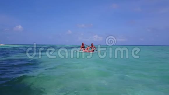 V08398两个漂亮的年轻女孩坐在冲浪板上在温暖的蓝色海水中鸟瞰视频的预览图