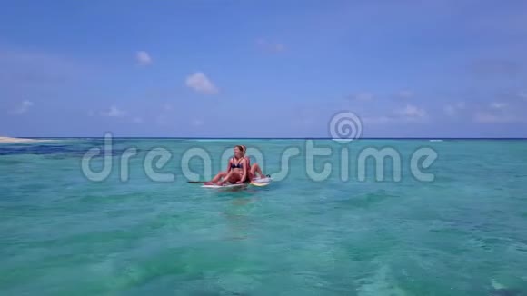 V08383两个漂亮的年轻女孩坐在冲浪板上在温暖的蓝色海水中鸟瞰天空视频的预览图