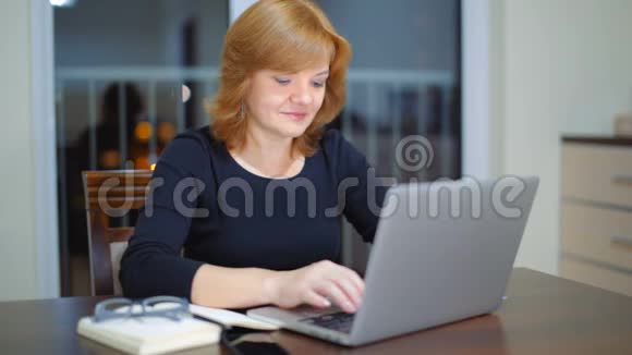 不错的成年女士晚上在家使用笔记本电脑打字视频的预览图