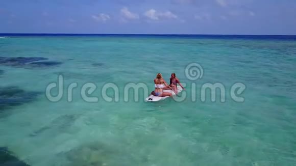 V08187两个漂亮的年轻女孩坐在冲浪板上在温暖的蓝色海水中鸟瞰天空视频的预览图