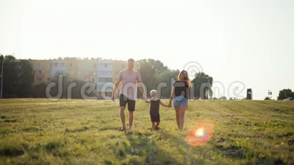 幸福的年轻家庭走在草地上牵着小儿子的手视频的预览图