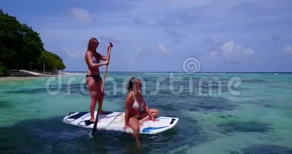 V08239两个漂亮的年轻女孩坐在冲浪板上在温暖的蓝色海水中鸟瞰天空视频的预览图