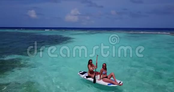 V08278两个漂亮的年轻女孩坐在冲浪板上在温暖的蓝色海水中鸟瞰天空视频的预览图