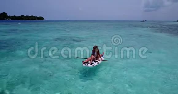 V08309两个漂亮的年轻女孩坐在冲浪板上在温暖的蓝色海水中鸟瞰天空视频的预览图