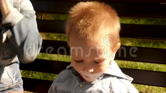 那个男孩坐在公园的长凳上玩冰淇淋这孩子在冰淇淋里很脏快乐的肖像视频的预览图