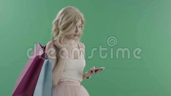 年轻的金发女人在智能手机上发短信等待着一个人拿着袋子对着绿色的屏幕视频的预览图