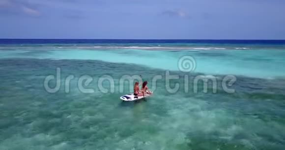 V08288两个漂亮的年轻女孩坐在冲浪板桨板上在温暖的蓝色海水中鸟瞰视频的预览图