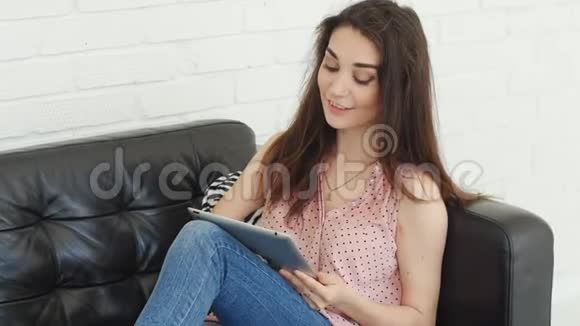 年轻的高加索女人坐在沙发上使用平板电脑视频的预览图