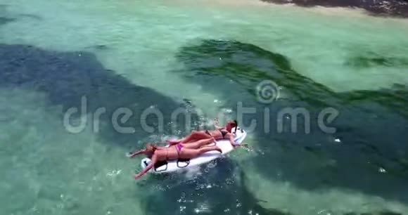 V08172两个年轻漂亮的女孩坐在冲浪板上在温暖的蓝色海水中俯瞰空中景色视频的预览图
