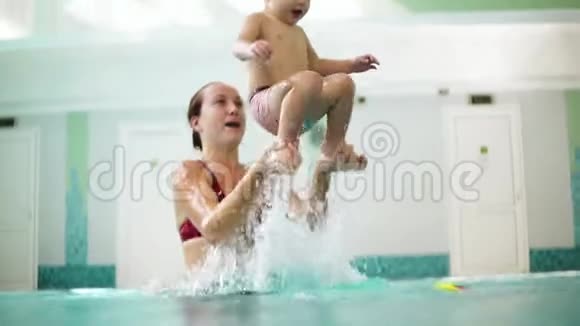 年轻的母亲正在把儿子从水里抱起来一边教他如何在游泳池里游泳视频的预览图