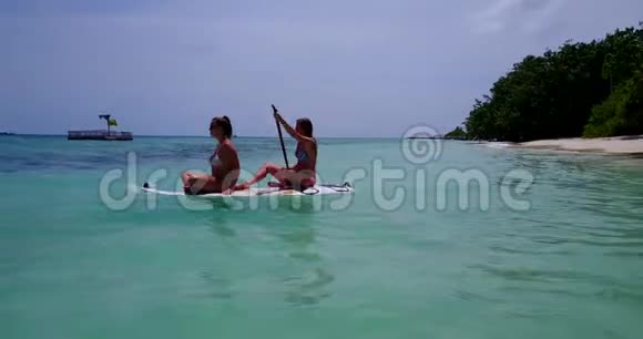 V08313两个漂亮的年轻女孩坐在冲浪板上在温暖的蓝色海水中鸟瞰天空视频的预览图