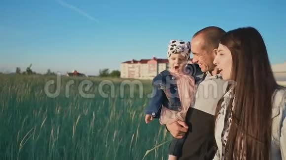 一个幸福的家庭三个人沿着麦田走在绿色的小穗之间在远处城市建筑视频的预览图