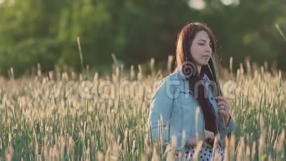 年轻漂亮的女孩一头乌黑的长发在一片麦田里在绿色的小穗中享受着大自然和夏天自由视频的预览图