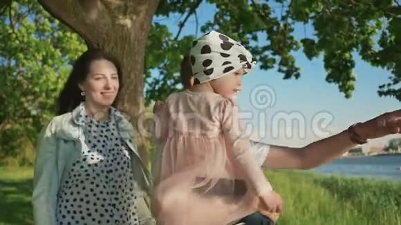 一个年轻的家庭和一个小女儿在湖边的一棵树下的公园里他父亲把女儿抱在视频的预览图