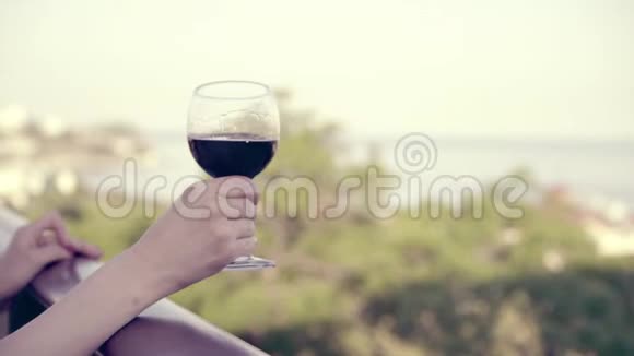 女子手捧一杯红酒在酒庄露台上观海女孩慢慢地摇晃着杯子视频的预览图