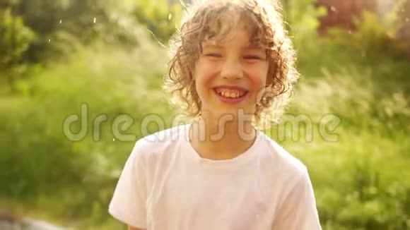一个美丽的卷发男孩站在夏天温暖的雨下微笑着儿童节节日快乐视频的预览图