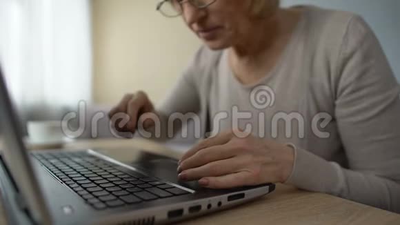 老妇人在家里慢慢地在笔记本电脑上打字学习电脑课程在线培训视频的预览图