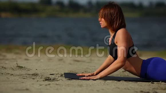 海滩上的女孩确实锻炼了瑜伽中的眼镜蛇姿势水平布线特写视频的预览图