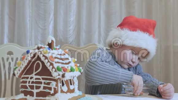 圣诞老人的帽子里可爱小男孩在厨房用巧克力剥下一颗糖果视频的预览图