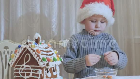 圣诞老人帽子里可爱小男孩在厨房里吃巧克力糖视频的预览图