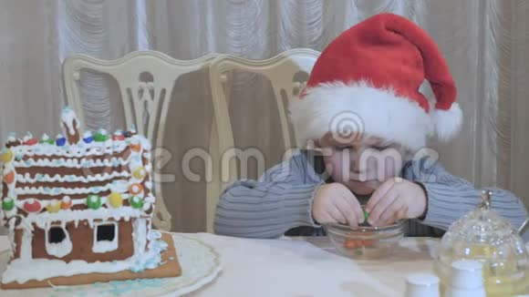 圣诞老人帽子里可爱的小男孩桌上放着五颜六色的糖果视频的预览图