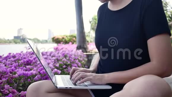 美丽的亚洲年轻女子坐在公园的长凳上用笔记本电脑视频的预览图