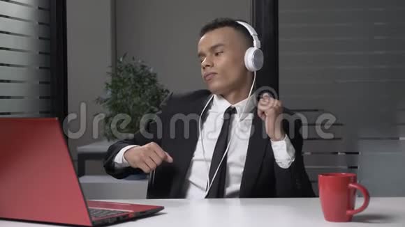 年轻成功的非洲商人西装革履戴着耳机在电脑上听音乐在办公室里跳舞60视频的预览图