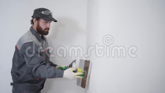一个留着胡须的成年建筑工人用一把长铲和石膏把墙对齐这个人把这幅画涂在视频的预览图