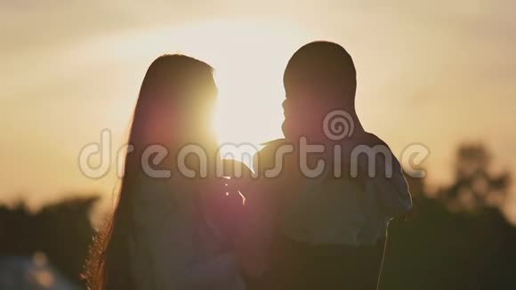 幸福的家庭在夕阳的照耀下爸爸妈妈有一个女儿在他们的手上玩和吻她爸爸快乐地长大视频的预览图