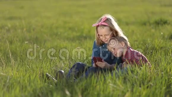 可爱的孩子坐在草地上玩智能手机视频的预览图