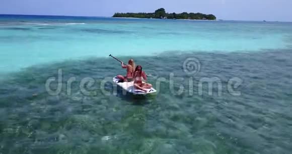 V08324两个漂亮的年轻女孩坐在冲浪板上在温暖的蓝色海水中鸟瞰天空视频的预览图
