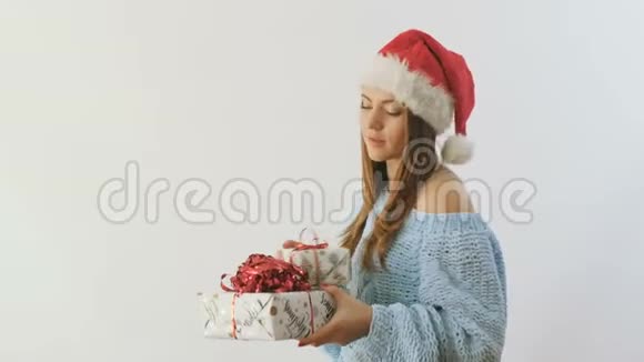 戴着圣诞老人帽子和礼物的快乐女孩在白色背景下竖起大拇指视频的预览图