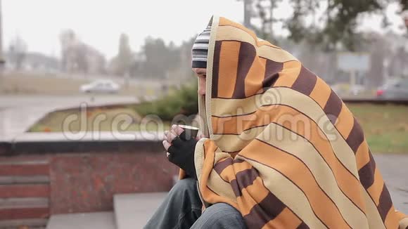 不快乐的男人独自坐在寒冷的街道上用咖啡和毯子取暖视频的预览图