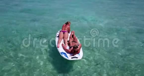 V08392两个漂亮的年轻女孩坐在冲浪板桨板上在温暖的蓝色海水中天空视频的预览图