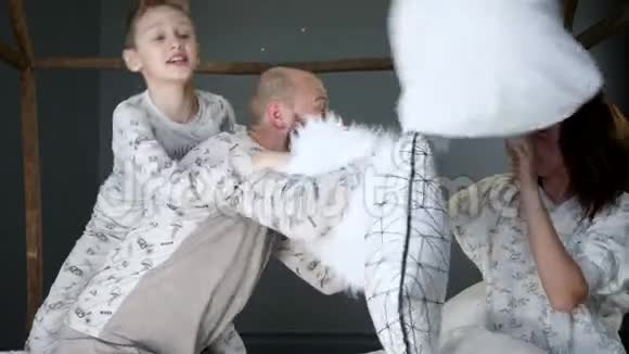 父母带着一个孩子在卧室里穿着相同的睡衣抱着枕头在床上胡闹视频的预览图