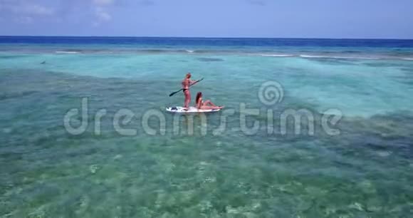 V08331两个漂亮的年轻女孩坐在冲浪板上在温暖的蓝色海水中鸟瞰天空视频的预览图